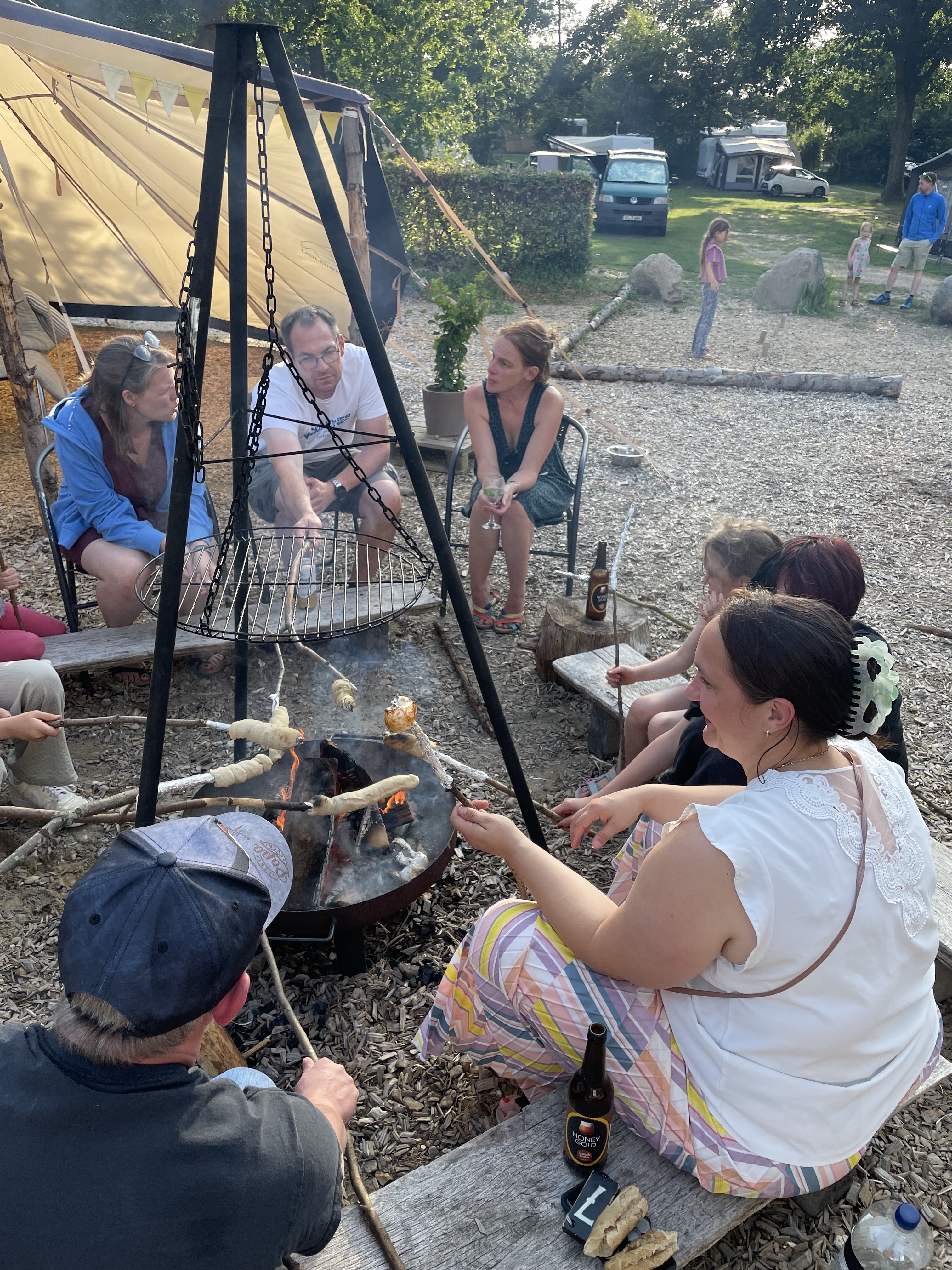 Mennesker sidder rundt om bålet en sommeraften og laver snobrød.
