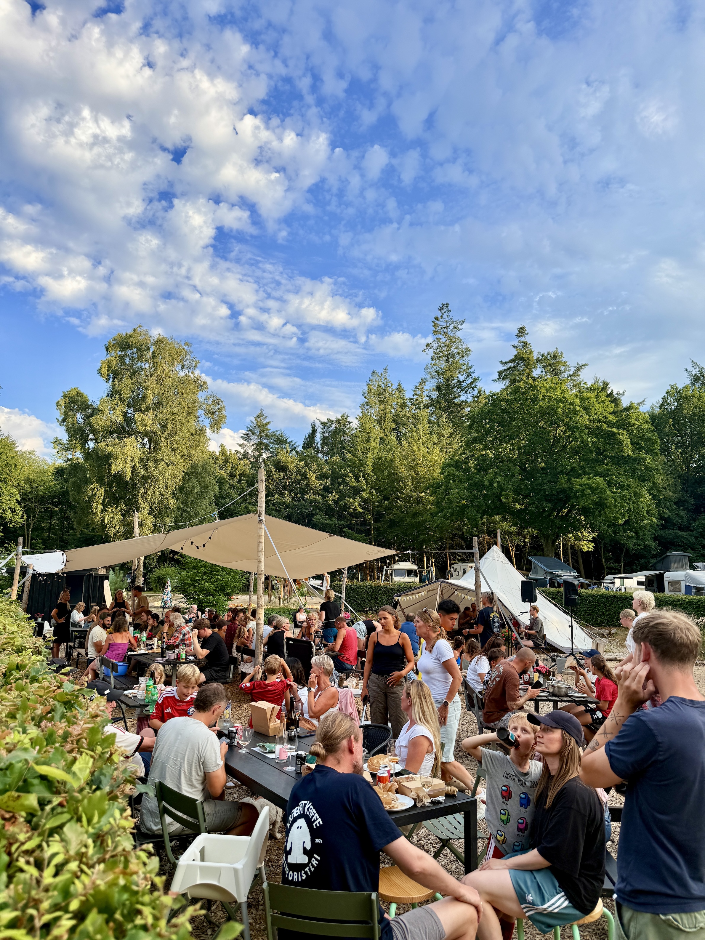Fællespladsen på Ly en sommerdag med mennesker, musik, bål og mad. 